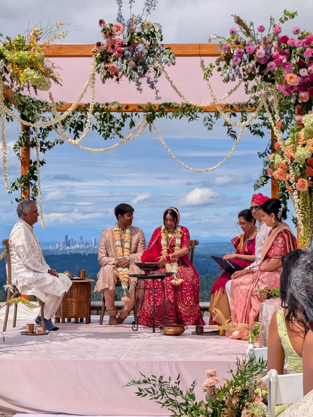The couple seated at the sacred fire during the ceremony, with family beside them and the city in the distance